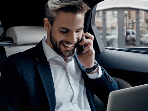 Man in backseat of a car on a mobile and laptop